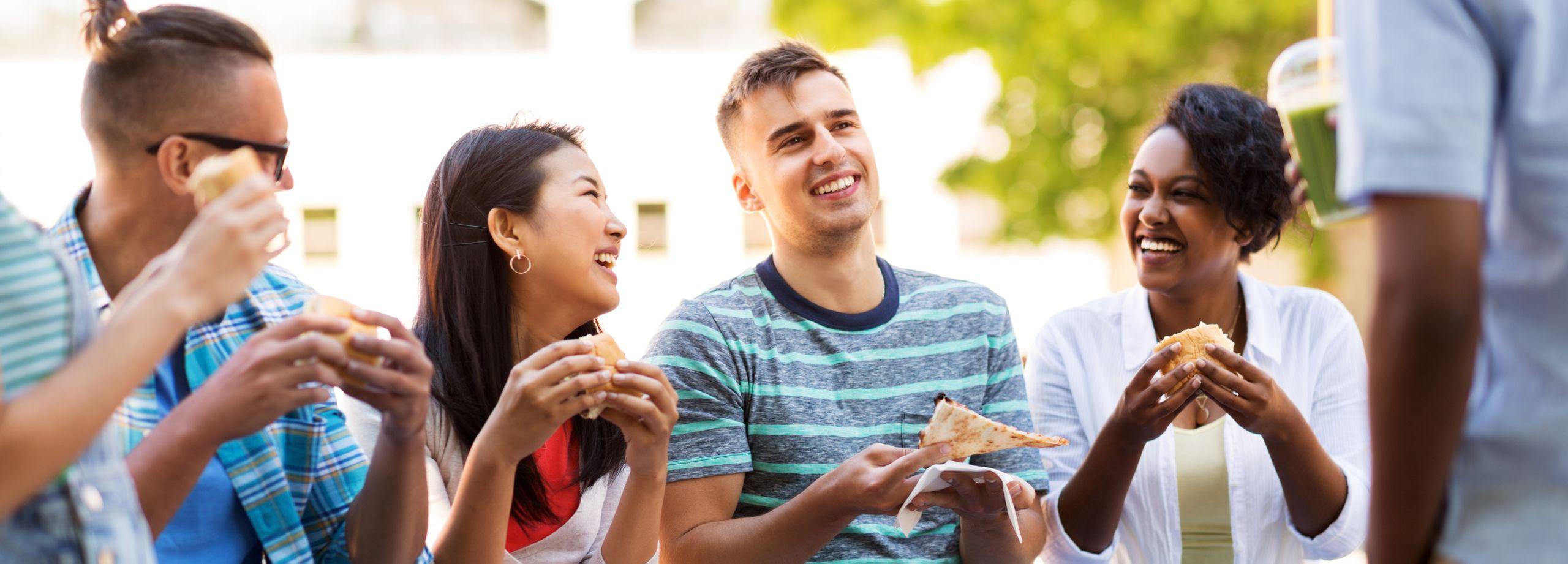 Group of friends outdoors laughing and eating pizza and sandwiches